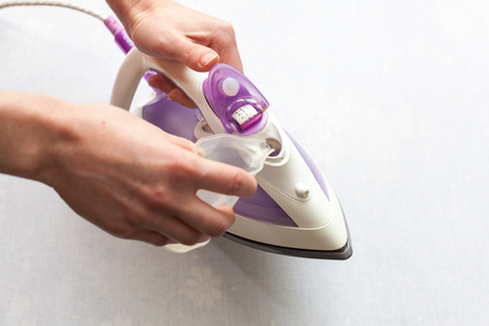 The girl pours distilled water into the tank of flat-iron. Top view during houseworkの写真素材