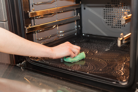 Housework and housekeeping concept. Scrubbing the stove and oven. Female hand with green sponge cleaning the kitchen ovenの写真素材