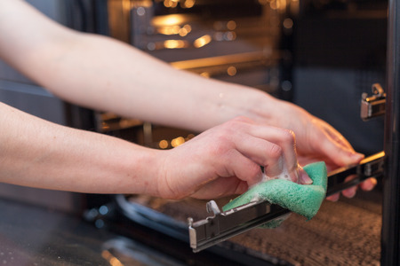 Housework and housekeeping concept. Scrubbing the stove and oven. Close up of female hand with green sponge cleaning the kitchen ovenの写真素材