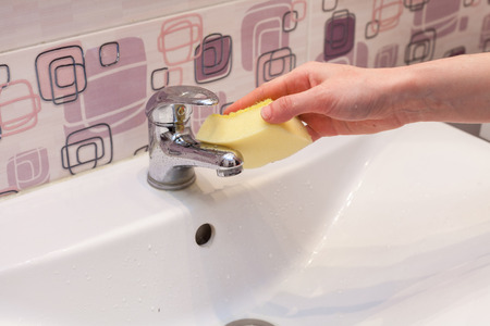Cleaning a new metal bathroom tap with yellow spongeの写真素材