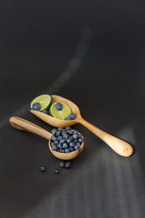 Fresh juicy blueberry fruits with limes on a wooden spoon against a dark backgroundの写真素材