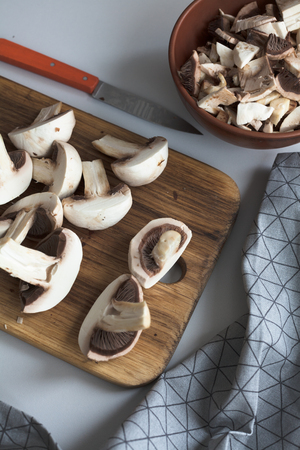 Fresh sliced mushrooms at wooden cutting board. Chopping food ingredients. Food background of fresh champignons at the old cutting board with copy spaceの写真素材