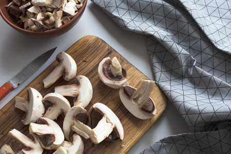 Fresh sliced mushrooms at wooden cutting board. Chopping food ingredients. Food background of fresh champignons at the old cutting board with copy space.の写真素材