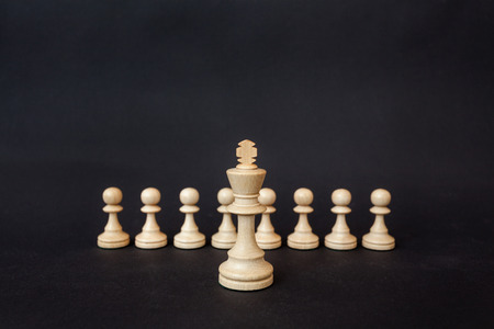 Chess pieces on a black background. The white king stands on the background of pawns.の写真素材