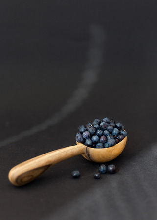 Fresh juicy blueberry fruits on a wooden spoon against a dark background.の写真素材