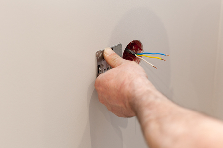 The hands of an electrician installing a wall power socketの写真素材