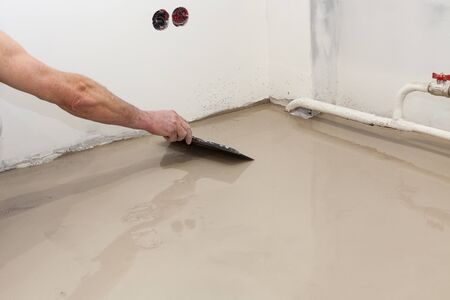 Repair work. Pouring floors in the room. Fill screed floor repair and furnish. Worker use a spatula to level the solution.の写真素材
