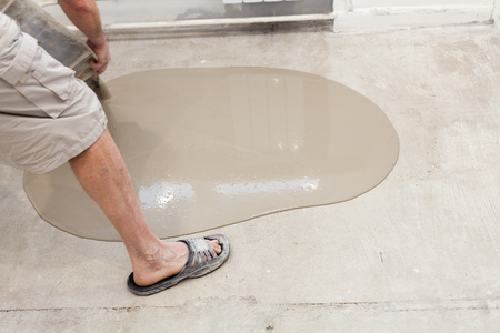Repair work. Pouring floors in the room. Fill screed floor repair and furnish. Worker pouring concrete on the floor.の写真素材