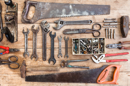 Composition of construction tools on an old battered wooden surface of tools: pliers, pipe wrench, screwdriver, hammer, metal shears, saws.の写真素材