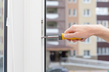 Handyman repairs plastic window with screwdriver. Workman adjusts the operation of the plastic window.の写真素材