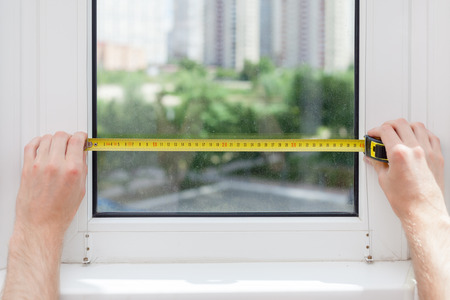 The employee makes a measurement of the glass in a plastic window using a tape measure.の写真素材