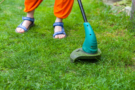 Garden equipment. Young woman mowing the grass with a trimmerの写真素材