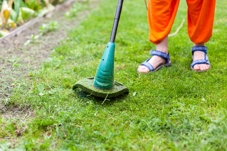 Garden equipment. Young woman mowing the grass with a trimmerの写真素材