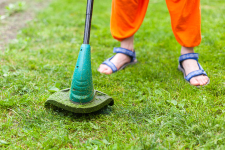 Garden equipment. Young woman mowing the grass with a trimmerの写真素材