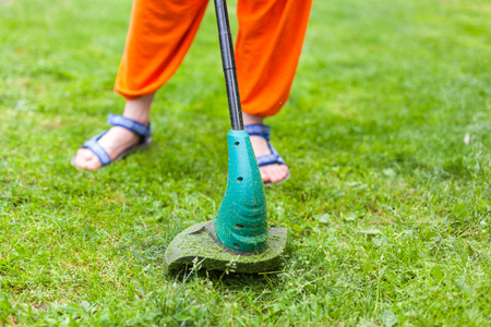Garden equipment. Young woman mowing the grass with a trimmerの写真素材