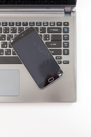 Broken smartphone with cracked screen lay on laptopの写真素材