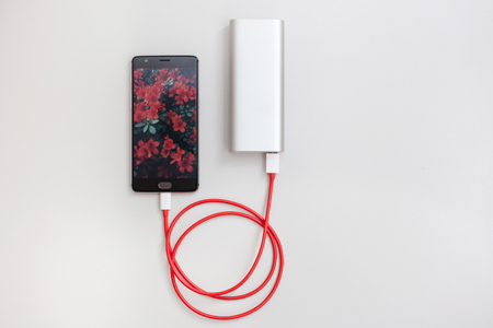 Smartphone charging with power bank on white tableの写真素材