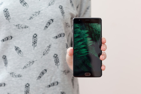 Selective focus, film effect. Young woman holding mobile phone with copy space, showing her black blank screen to the camera. People and technology. Woman show her smart phoneの写真素材