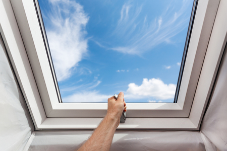 Man open new skylight (mansard window) in an attic room against blue skyの写真素材
