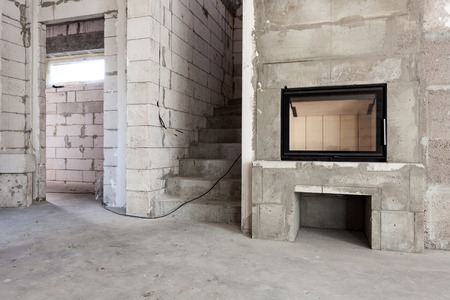 New house under construction. Modern wood-fired fireplace construction. Aerated concrete blocks, cement brickwork walls, plastic window, electric wiring installation. Cement covering in empty roomの写真素材