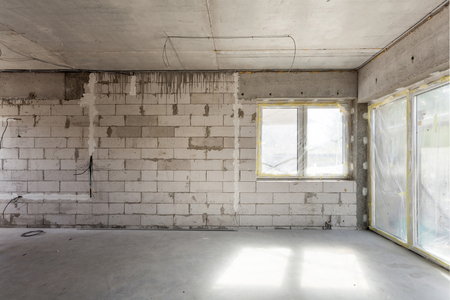 New house under construction. Aerated concrete blocks, cement brickwork walls, plastic window, electric wiring installation. Cement covering in empty roomの写真素材