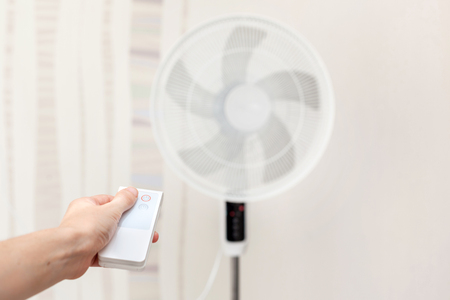White electric fan turns on, turns off with the remote control. Hand hold electric fan remote.の写真素材