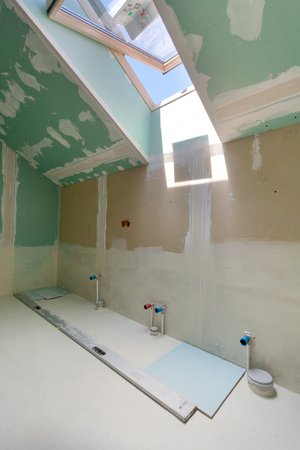 Finishing works at renovated apartment. Installation of pipes in bathroom with mansard windowの写真素材