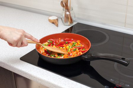 Vegetables are in a frying pan. Woman cooking colourful fresh vegetables on an electric stoveの写真素材