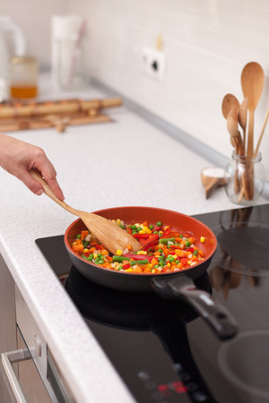 Vegetables are in a frying pan. Woman cooking colourful fresh vegetables on an electric stoveの写真素材