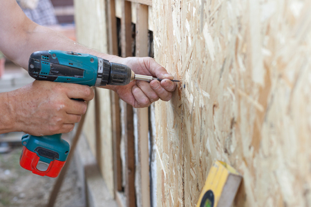 Construction worker use screwdriver to attach Wood Particle Board (fiberboard) to the wallの写真素材