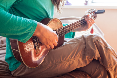 Closeup of a young man's hands playing an acoustic guitar ukulele at the home. Man holding ukuleleの写真素材