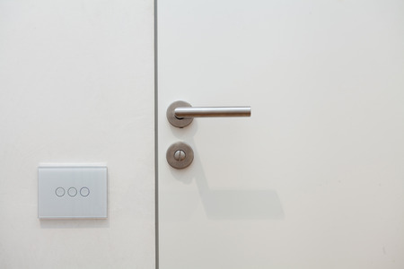 Light switch next to the door handle. Open white door with metallic handle.の写真素材