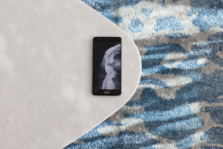 Modern white stool made of artificial stone stands on a carpet with fine nap, a top view. The mobile phone lies on a new chair.の写真素材