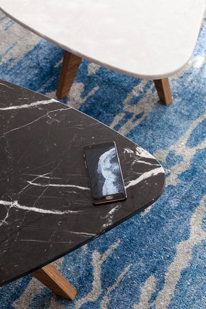 Two modern stool made of black and white artificial stone stands on a carpet with fine nap, a top view. The mobile phone lies on a new small chair.の写真素材