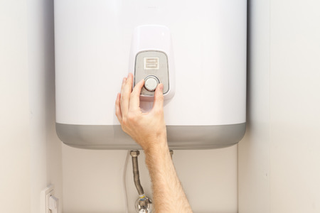 Close-up of man hands setting the temperature of water in Electric Boilerの写真素材