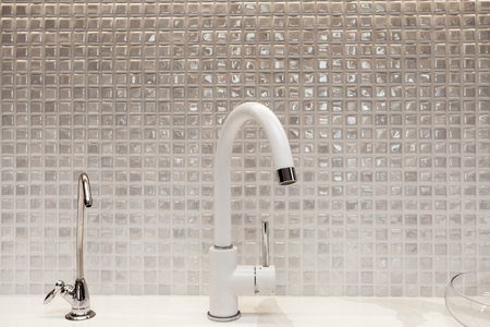 Modern designer chrome water tap over stainless steel kitchen sink. Interior of bright white kitchenの写真素材