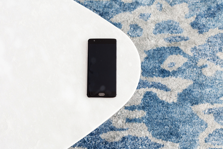 Modern white stool made of artificial stone stands on a carpet with fine nap, a top view. The mobile phone lies on a new chair. Composition, texture, color.の写真素材