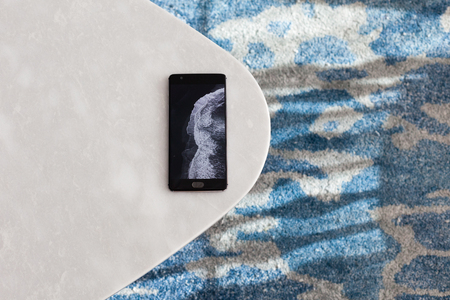 Modern whiteÐµ table made of artificial stone stands on a carpet with fine nap, a top view. The mobile phone lies on a new small table.の写真素材