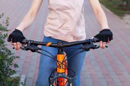 A girl in bicycle gloves holds her hand on the handlebars, clamping the brakes. A bicycle element on a street background.の写真素材
