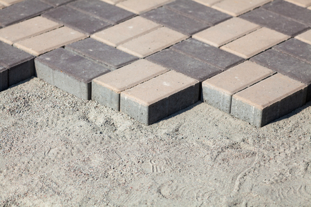 Gray paving blocks - side view. New sidewalk with rectangular stones. Paving tiles in the process of laying.の写真素材