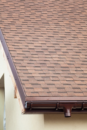 Roof under construction with new asphalt tile roof and rain gutterの写真素材