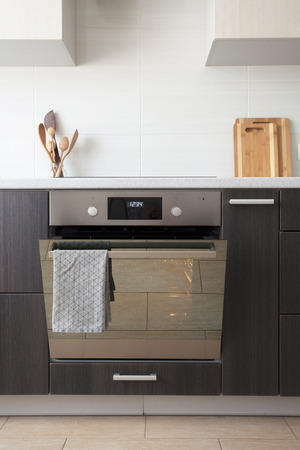 New light kitchen with ceramic hob and empty open electric oven with hot air ventilation. Oven door with grey towel hanging on itの写真素材