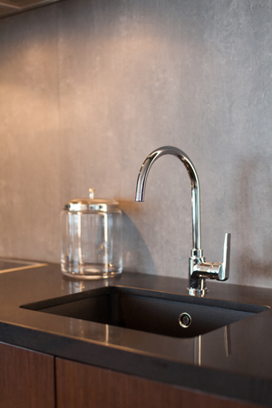 Detail of a rectangular designer kitchen sink with chrome water tap against a gray textured wallの写真素材