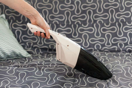 Young woman using a small manual vacuum cleaner while cleaning textile upholstery on the couch.の写真素材
