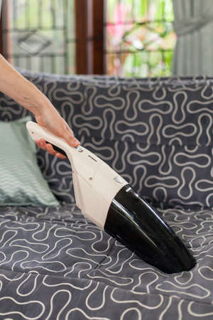 Young woman using a small manual vacuum cleaner while cleaning textile upholstery on the couch.の写真素材