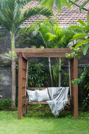 Classic outdoor wooden swing in the green garden with pillows and blanketの写真素材