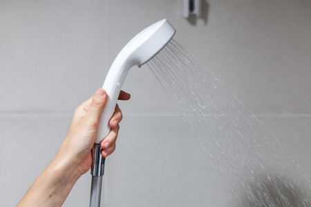 Housewife holds in her hand cleen and closed off rain shower head in the bathroom.の写真素材