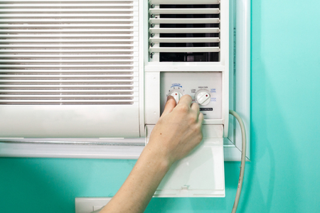 The girl regulates the temperature of a small room air conditionerの写真素材