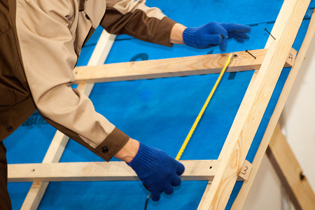 Worker with electric drill installing brown roof metal tile on wooden houseの写真素材
