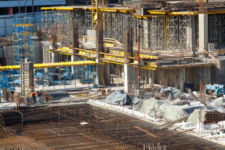 Construction of a large multi-storey commercial building. Builders work in overalls on the site pouring cement and concrete formwork, and tying the armature.の写真素材